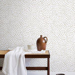 A bench with a towel and clay vases stands in front of a wall papered in a scalloped dot print in tan and white.