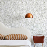 A modernist bed, hanging lamp and chair stand in front of a wall papered in a scalloped dot print in sage and white.