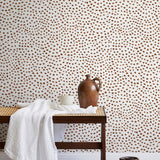 A bench with a towel and clay vases stands in front of a wall papered in a scalloped dot print in rust and cream.