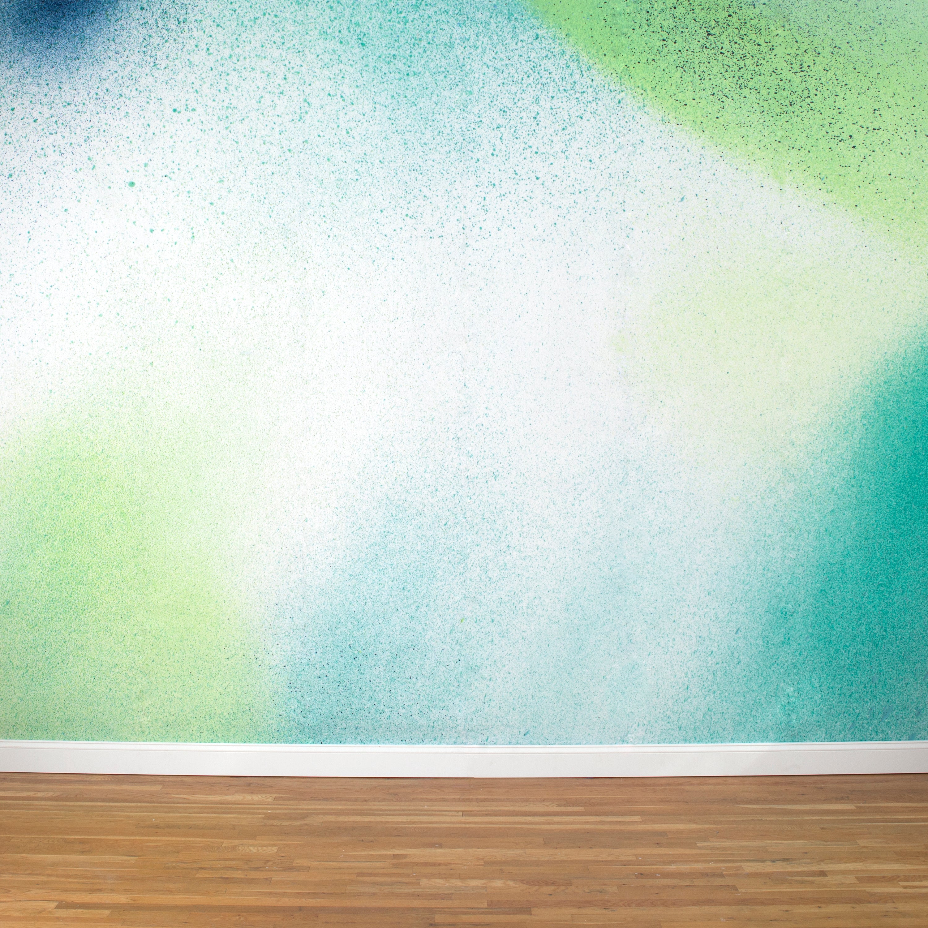 A wall mural in an abstract ombré paint splatter print in shades of green, turquoise and white.