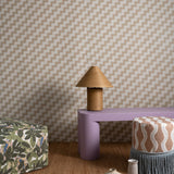 Several bolsters and a lamp sit in front of a wall papered in a playful zigzag stripe print in brown, gray and white.