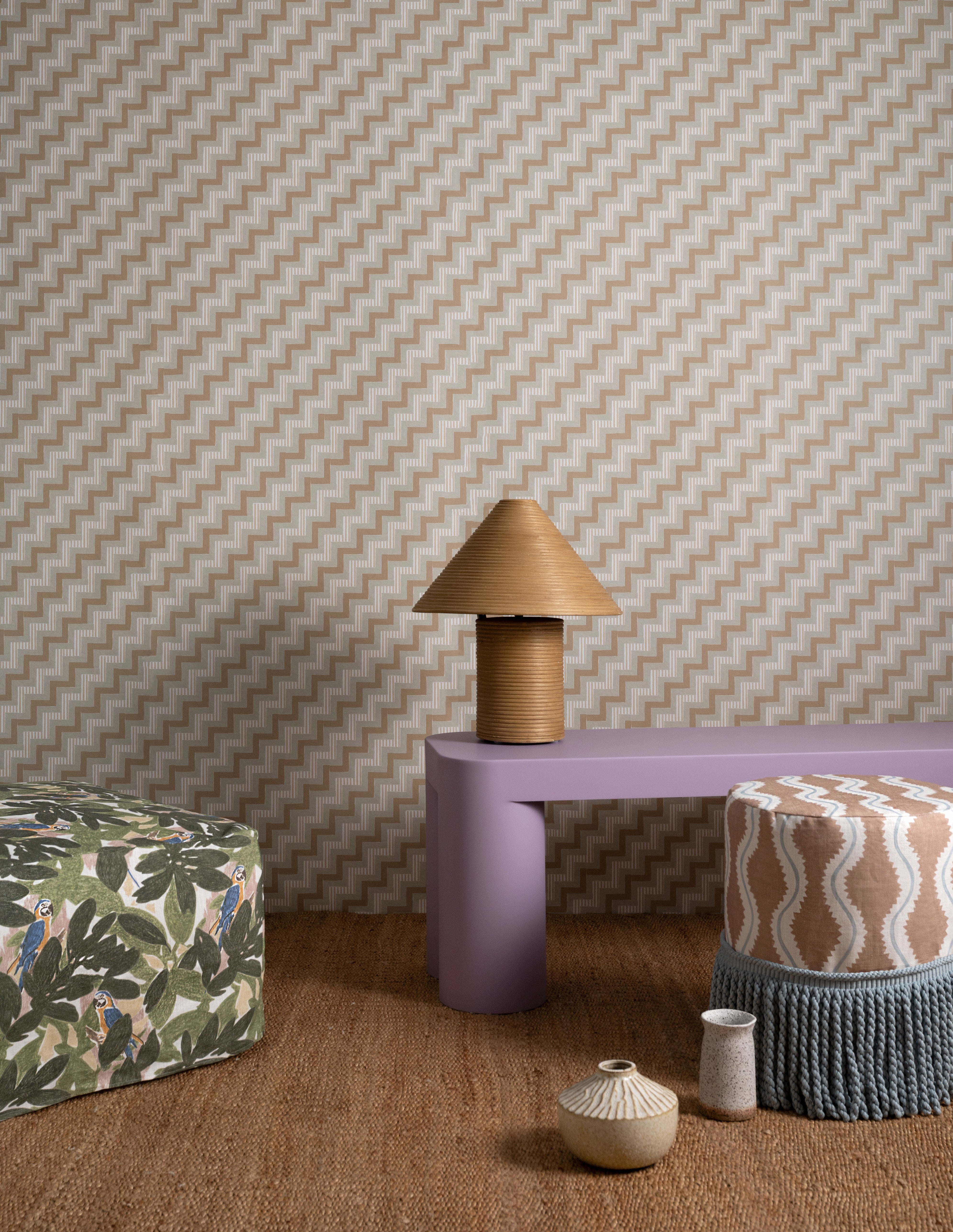 Several bolsters and a lamp sit in front of a wall papered in a playful zigzag stripe print in brown, gray and white.