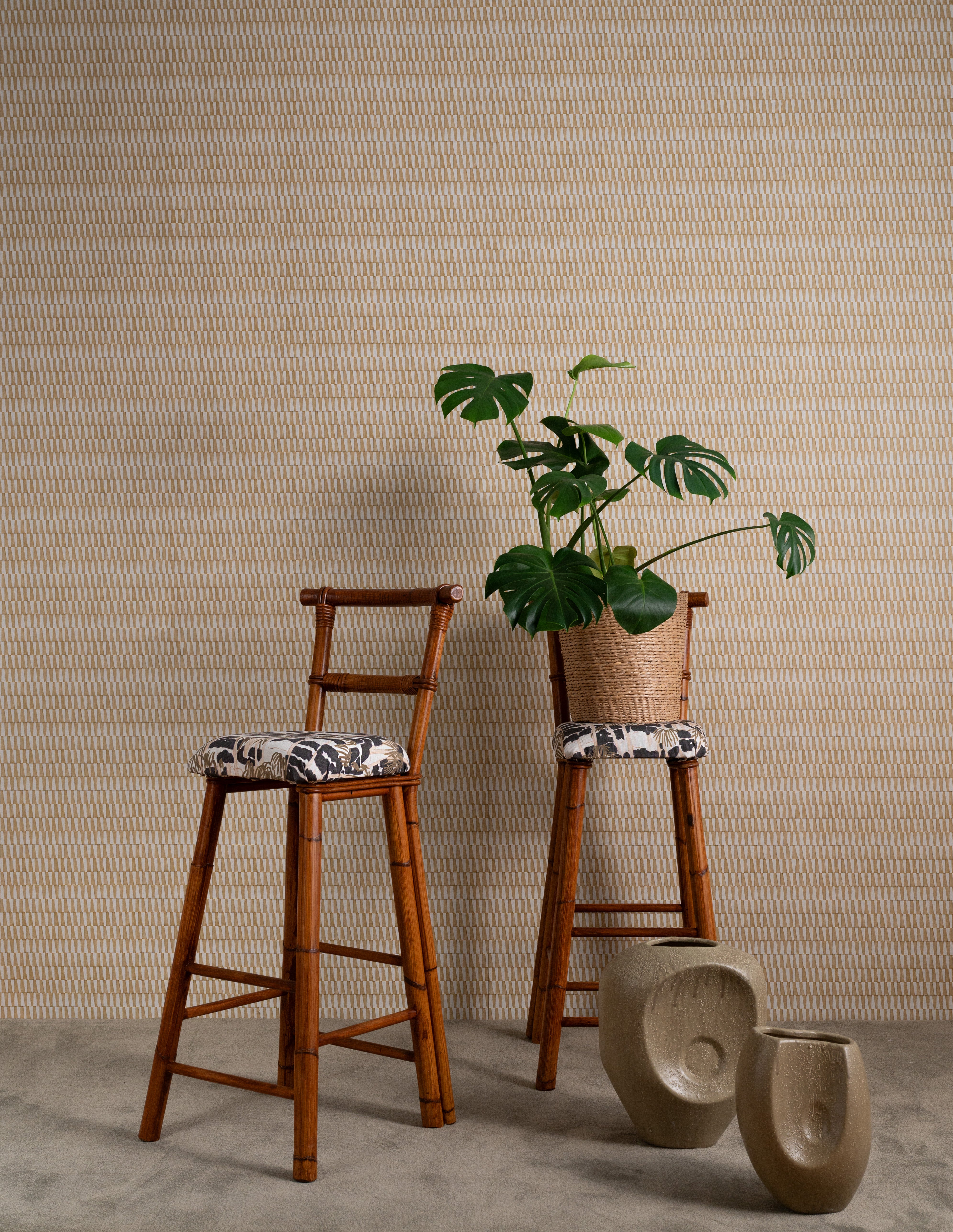 Two bamboo chairs with cushions upholstered in a painterly palm tree print. One has a potted plant on top.