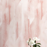 A vase of flowers stands in front of a wall papered in a linear geometric print in shades of pink and cream.