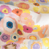 Close up of fabric yardage in a painterly floral print in multicolor pastels on a white field.