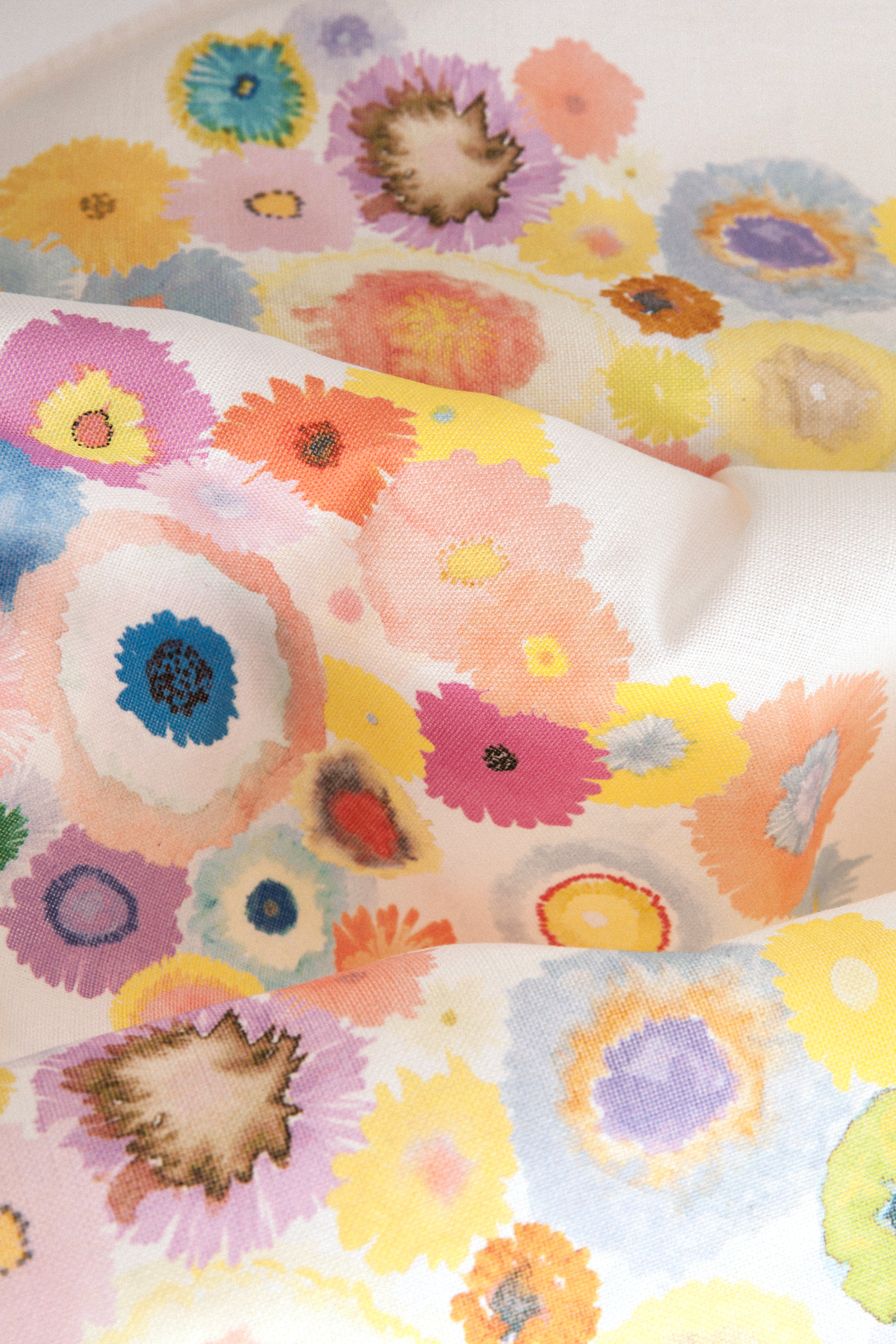 Close up of fabric yardage in a painterly floral print in multicolor pastels on a white field.