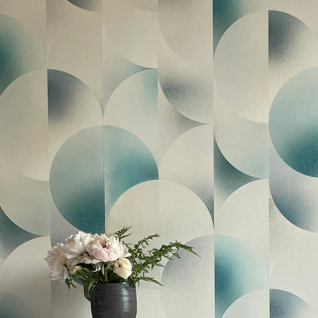 A vase of flowers stands in front of a wall covered in an abstract curvilinear print in mottled blue, gray and white.