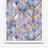 Partially unrolled wallpaper yardage in a painterly herringbone print in shades of blue, pink and orange.