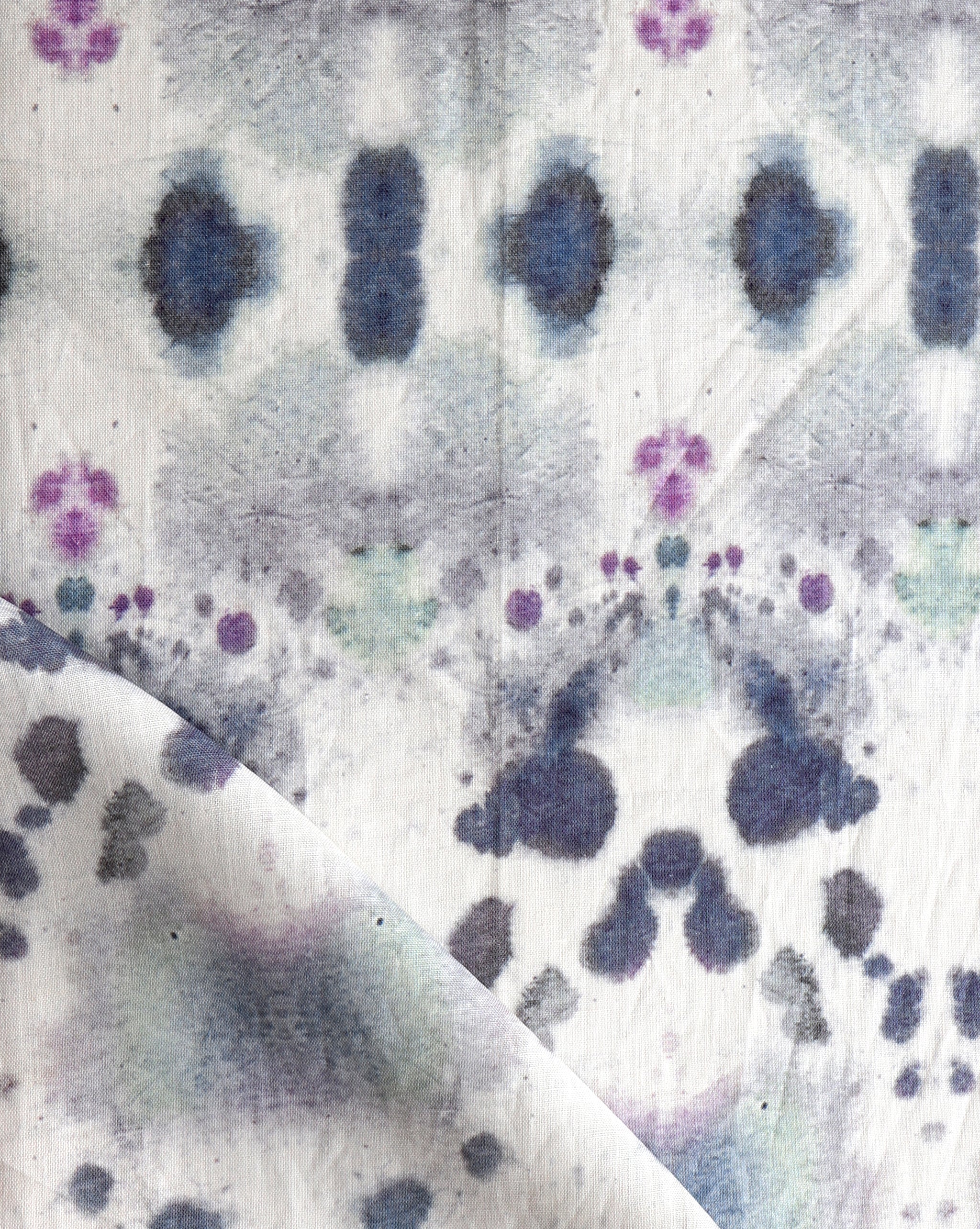 Draped fabric yardage in an abstract inkblot print in shades of purple and gray on a cream field.