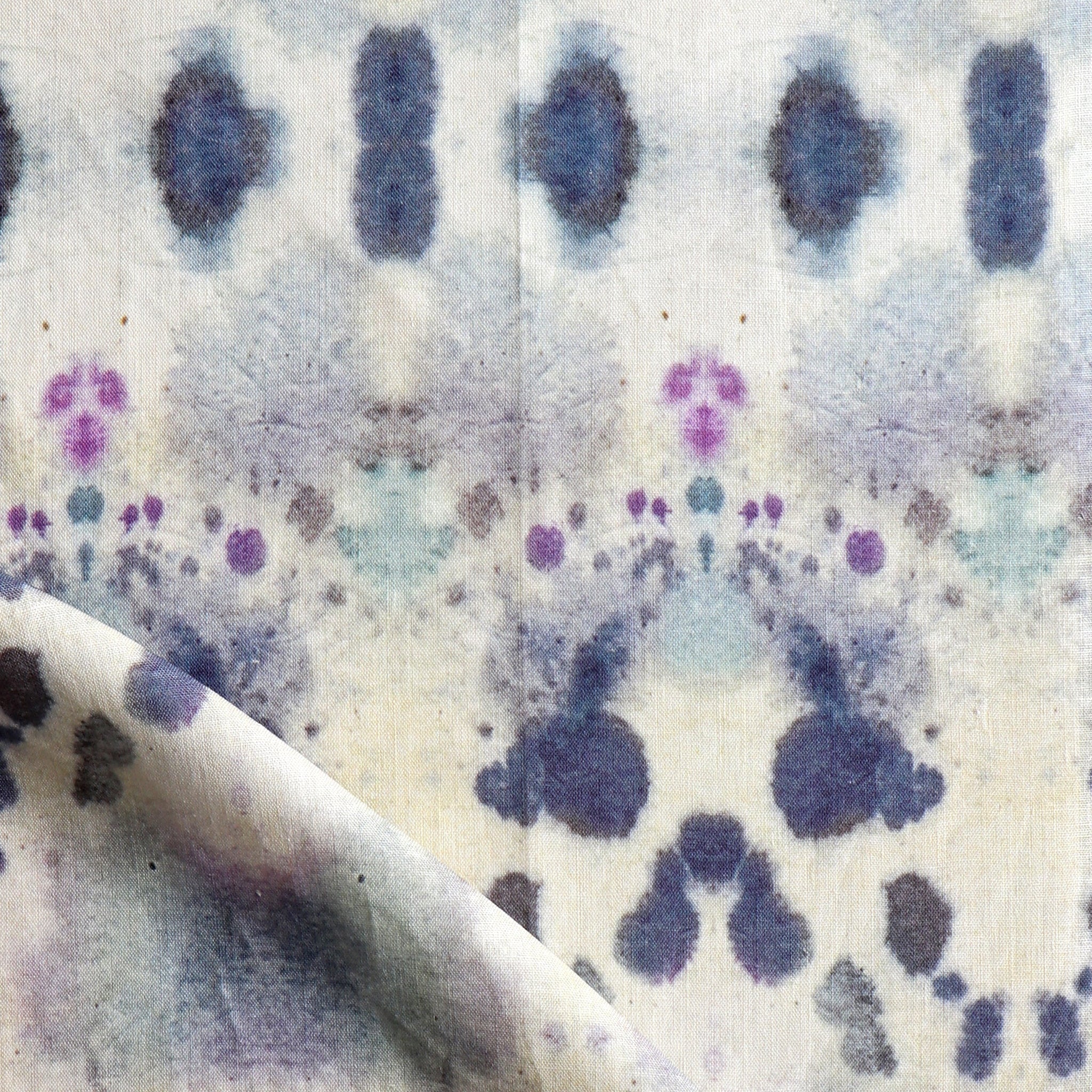 Draped fabric yardage in an abstract inkblot print in shades of blue and purple on a cream field.