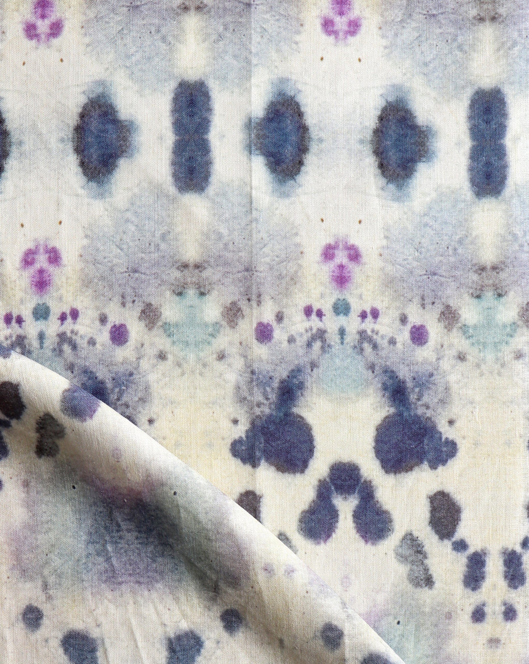 Draped fabric yardage in an abstract inkblot print in shades of blue and purple on a cream field.