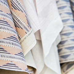 Folded, overlapping woven fabric swatches with geometric pastel prints in shades of pink, purple, blue and cream.