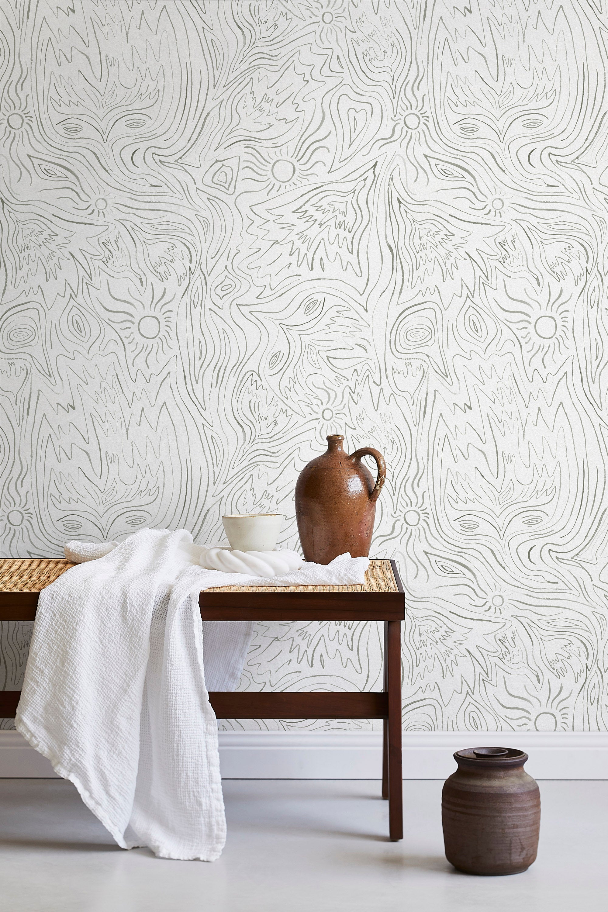 A bench with a towel and clay vases stands in front of a wall papered in a playful abstract sun print in gray and cream.