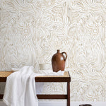 A bench with a towel and clay vases stands in front of a wall papered in a playful abstract sun print in brown and cream.