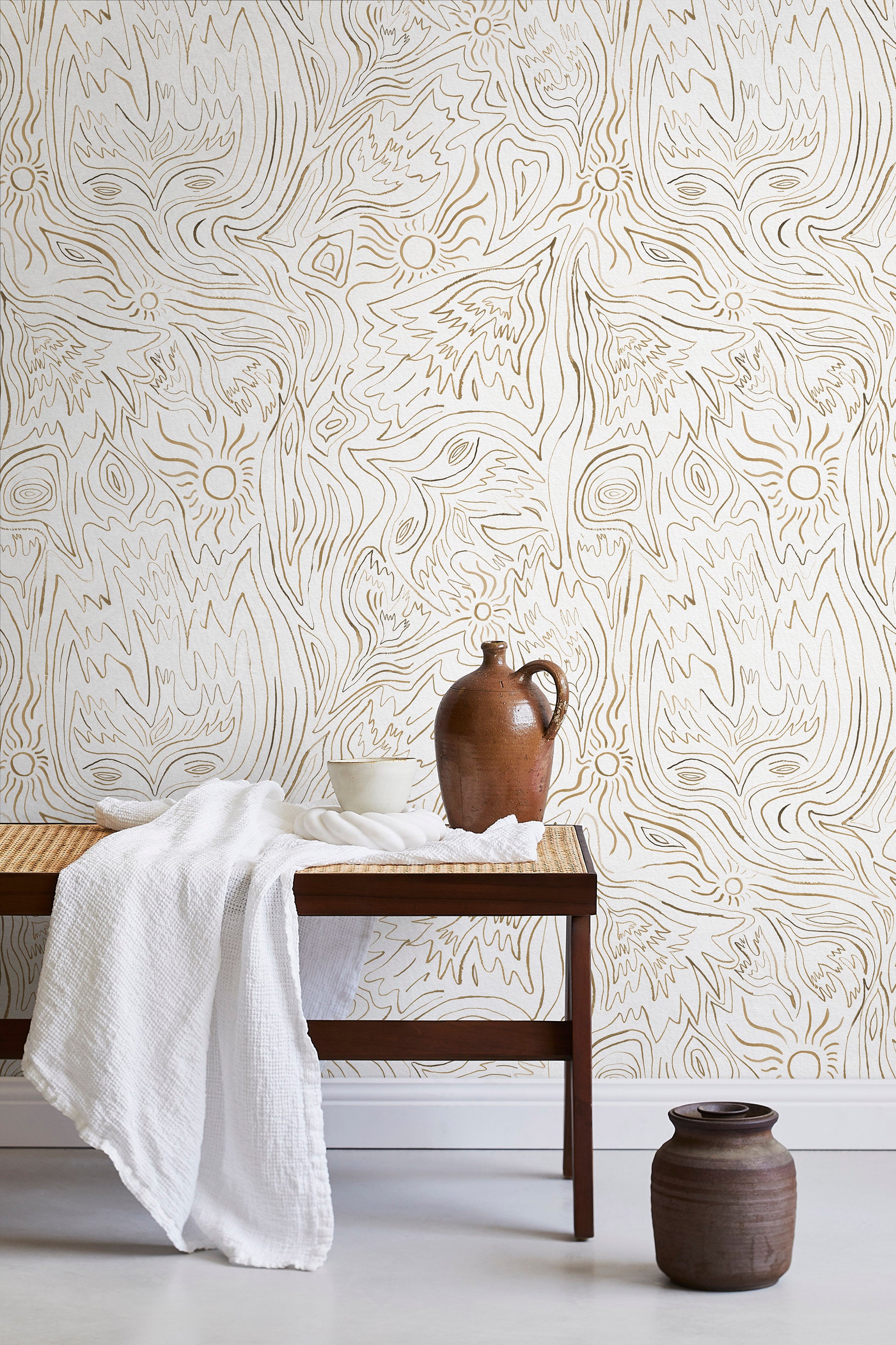 A bench with a towel and clay vases stands in front of a wall papered in a playful abstract sun print in brown and cream.