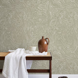 A bench with a towel and clay vases stands in front of a wall papered in a playful abstract sun print in white and tan.