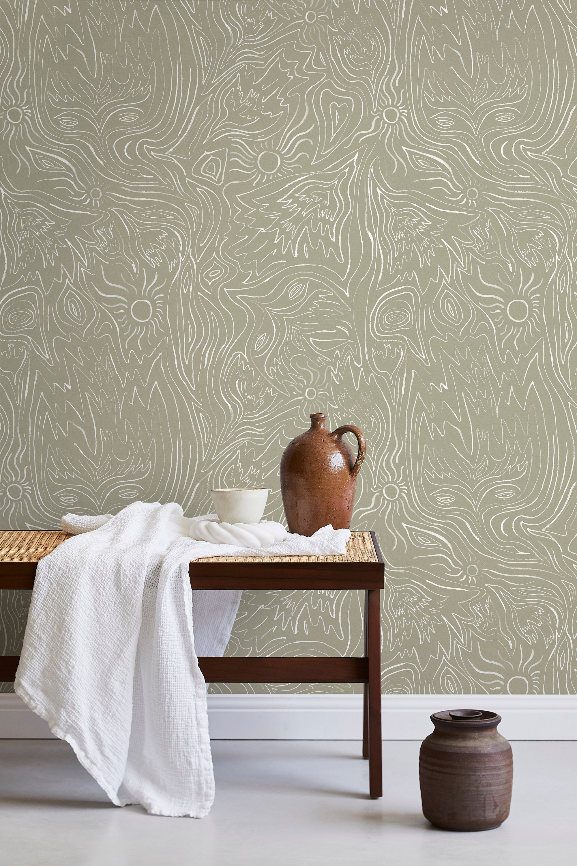 A bench with a towel and clay vases stands in front of a wall papered in a playful abstract sun print in white and tan.