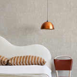 A modernist bed, hanging lamp and chair stand in front of a wall papered in a playful abstract sun print in white and cream.