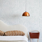 A modernist bed, hanging lamp and chair stand in front of a wall papered in an abstract sun print in light blue and white.