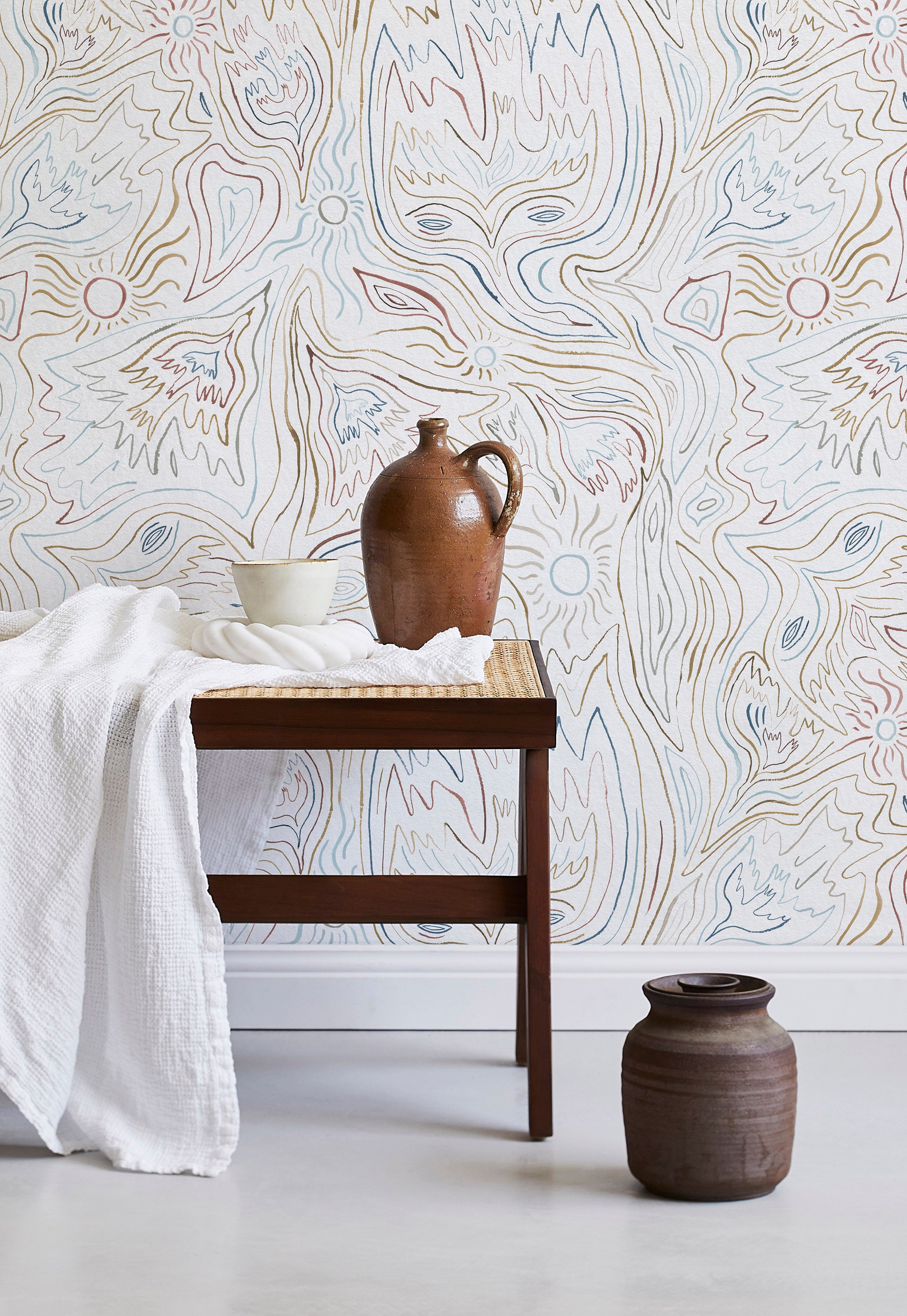 A bench with a towel and clay vases stands in front of a wall papered in an abstract sun print in brown, blue and white.