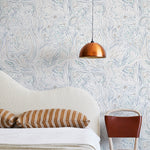 A modernist bed, hanging lamp and chair stand in front of a wall papered in an abstract sun print in brown, navy and white.