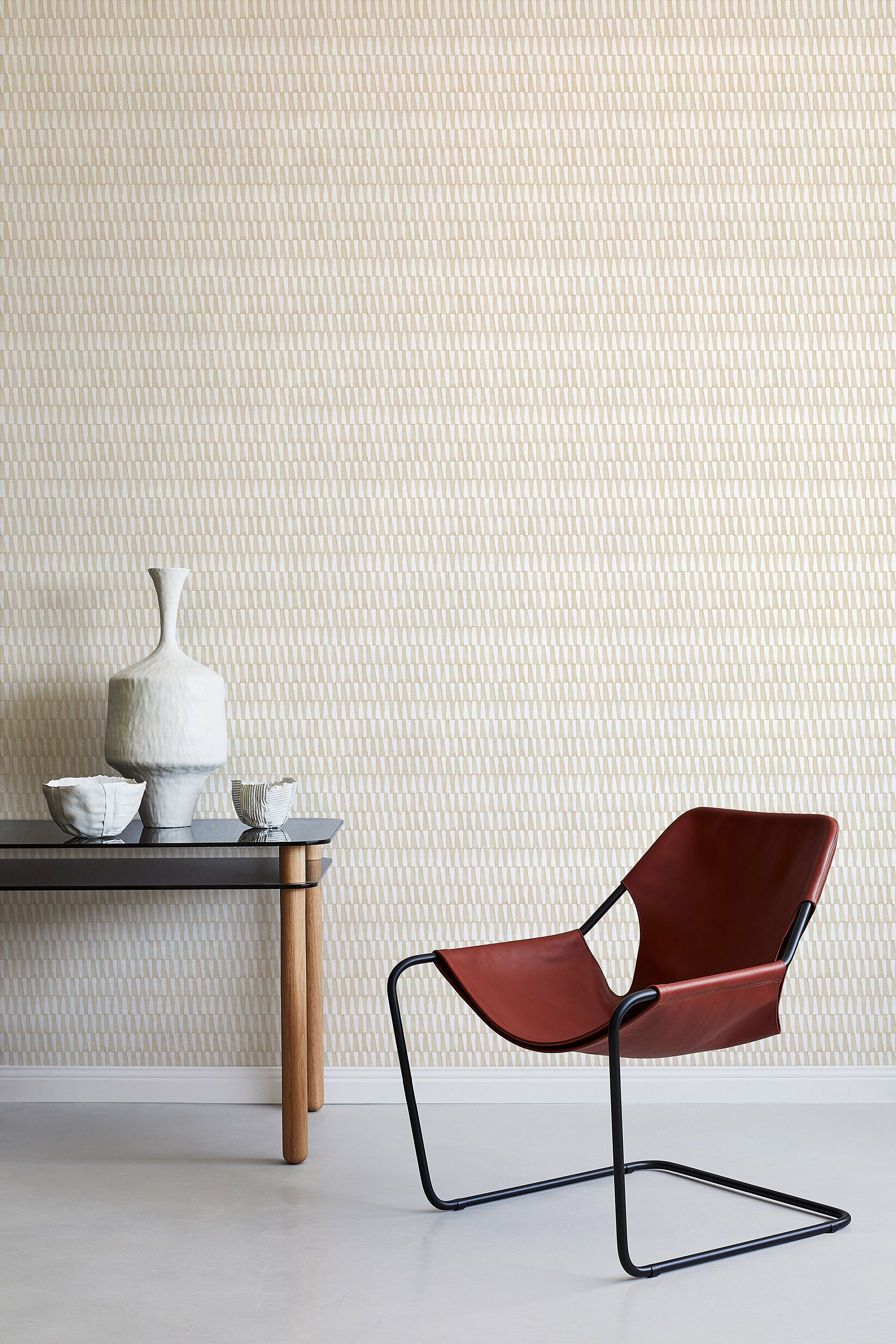 A modernist armchair stands in front of a wall papered in a playful triangular stripe print in white and light brown.