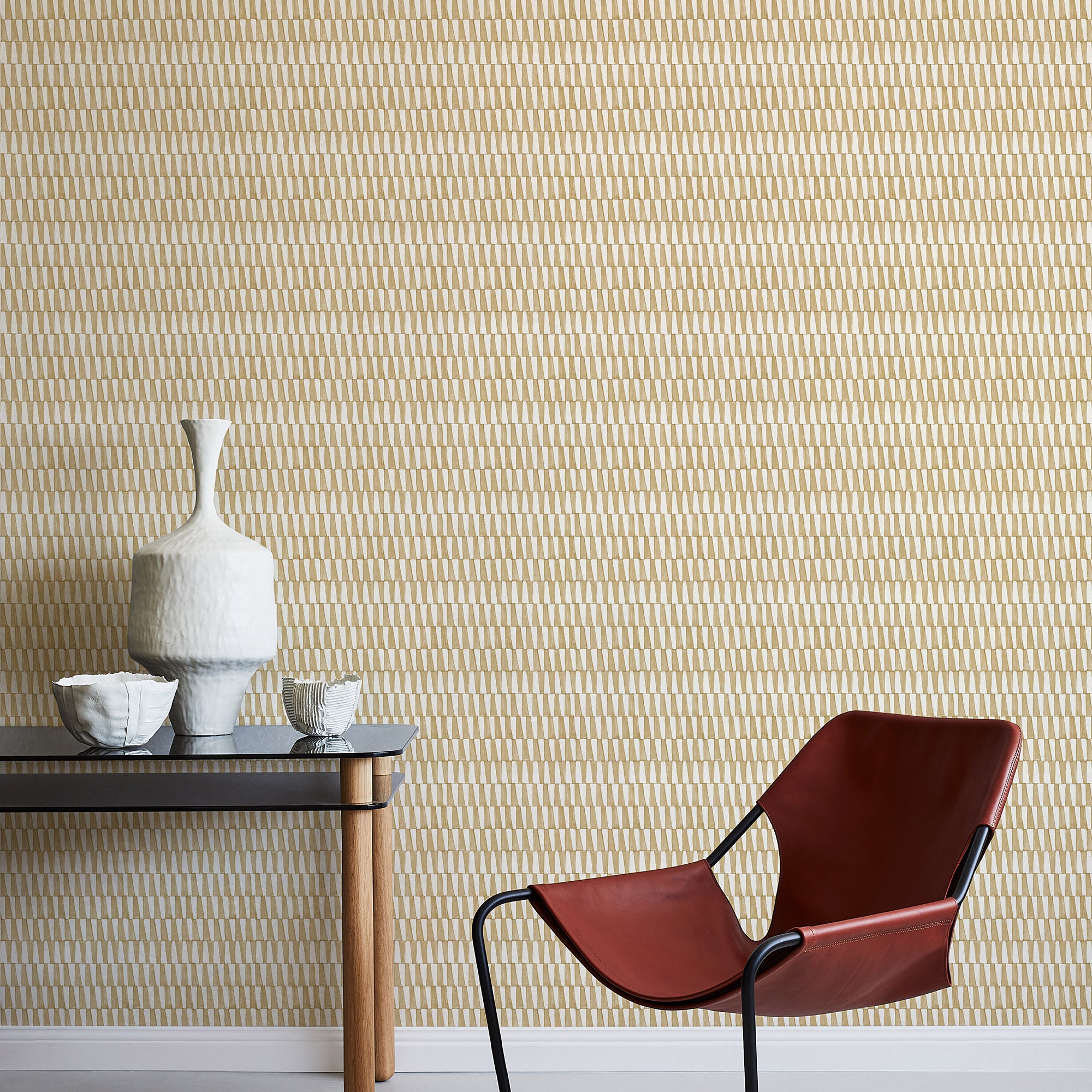 A modernist armchair stands in front of a wall papered in a playful triangular stripe print in tan and light brown.