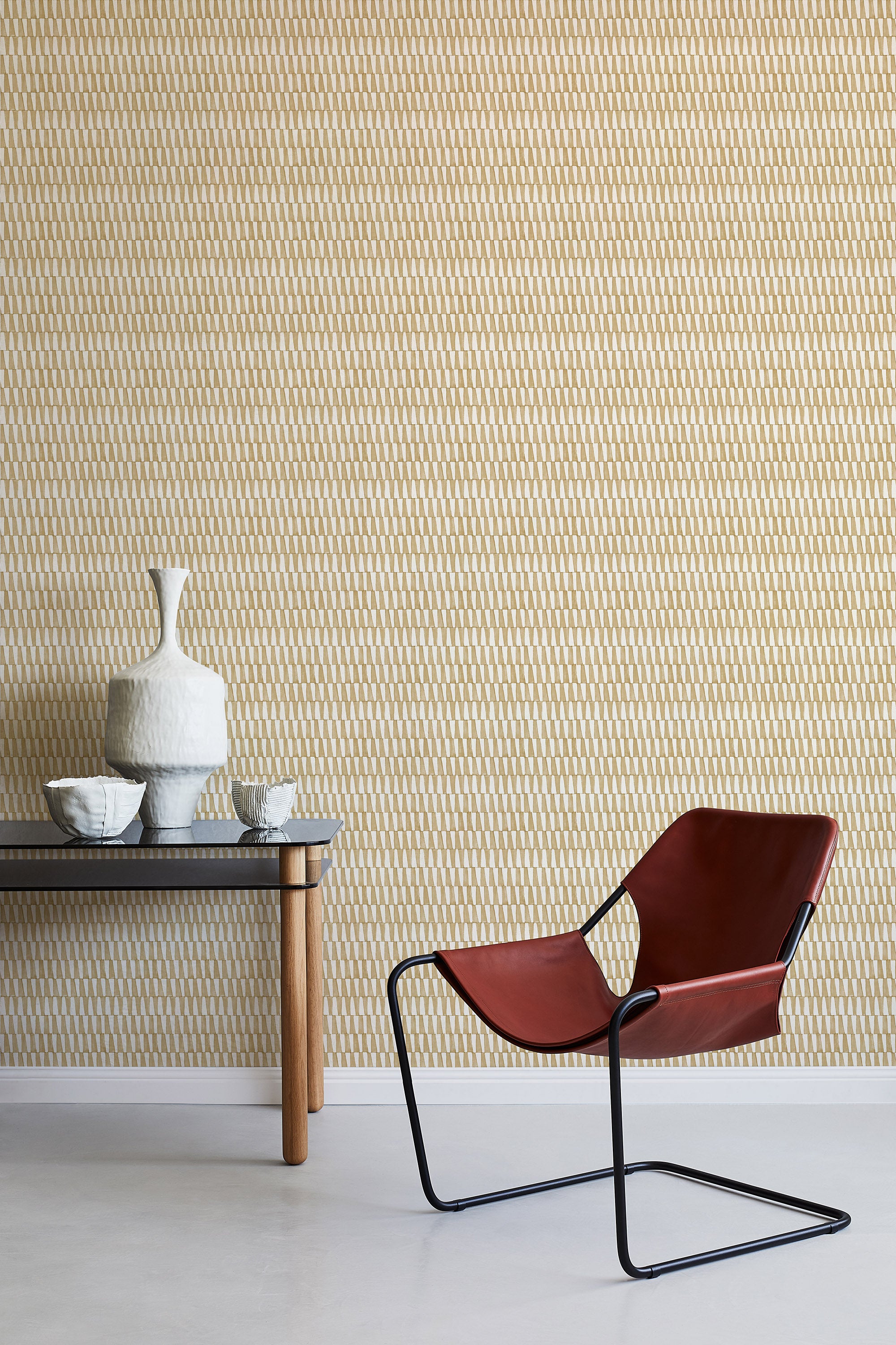 A modernist armchair stands in front of a wall papered in a playful triangular stripe print in tan and light brown.