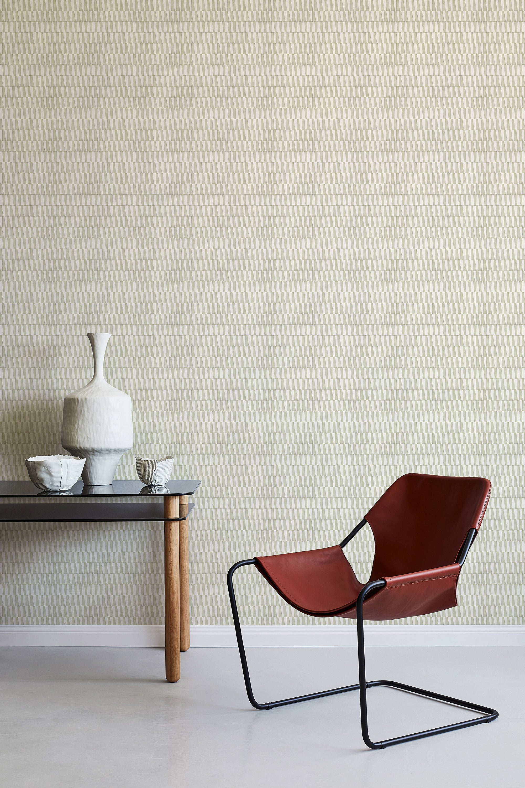 A modernist armchair stands in front of a wall papered in a playful triangular stripe print in gray and cream.