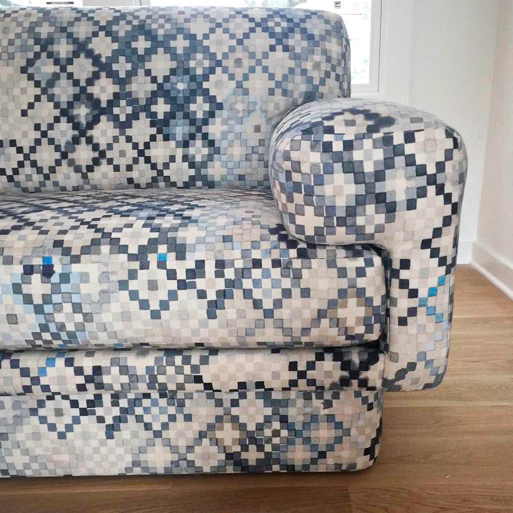 Detail of a sofa upholstered in a diamond checked pattern in shades of cream, gray and blue.