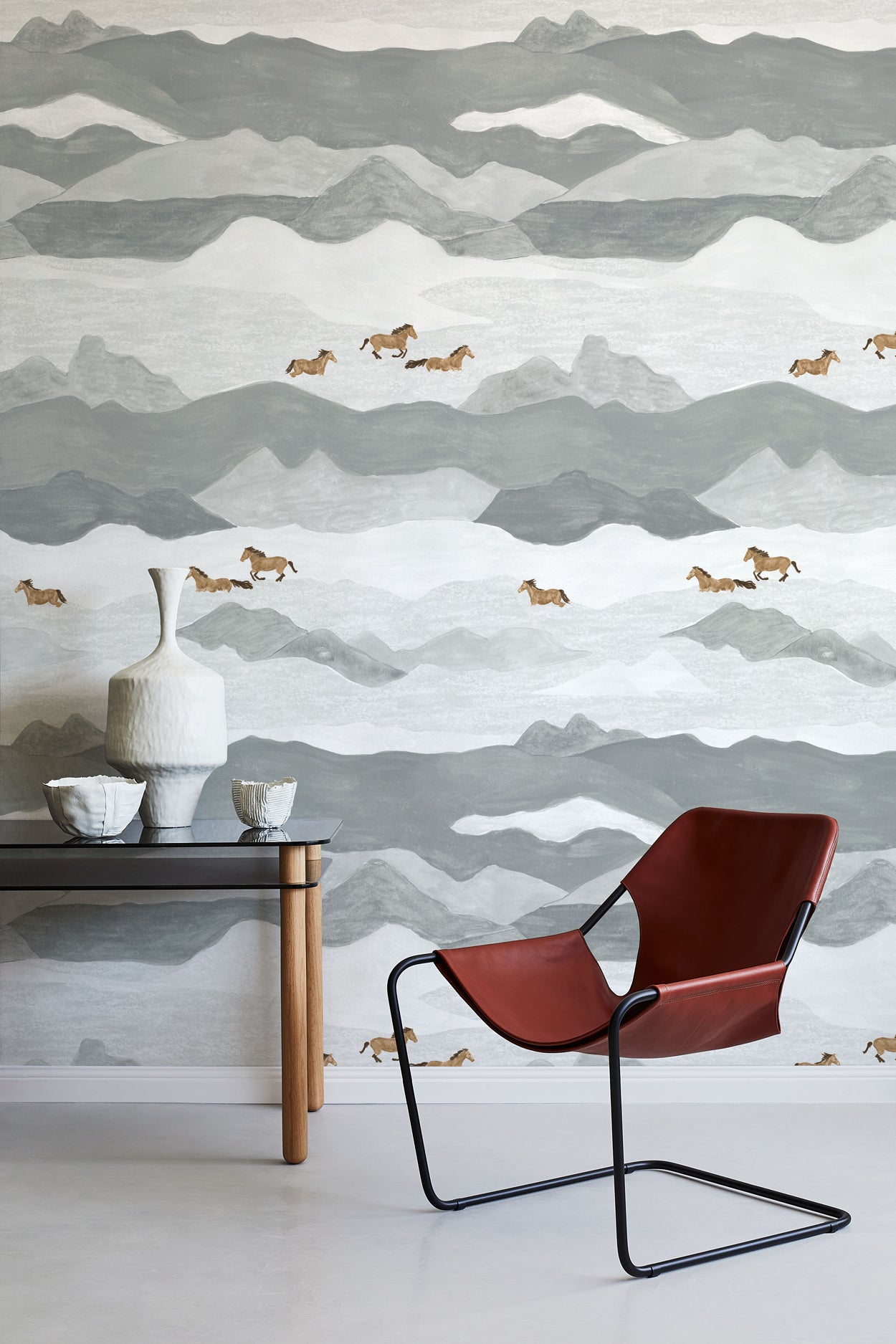 Room interior with a red chair, small table, and decorative items against a mountain-patterned wall.