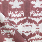 Draped fabric yardage in an abstract ikat print in shades of red and pink on a cream field.