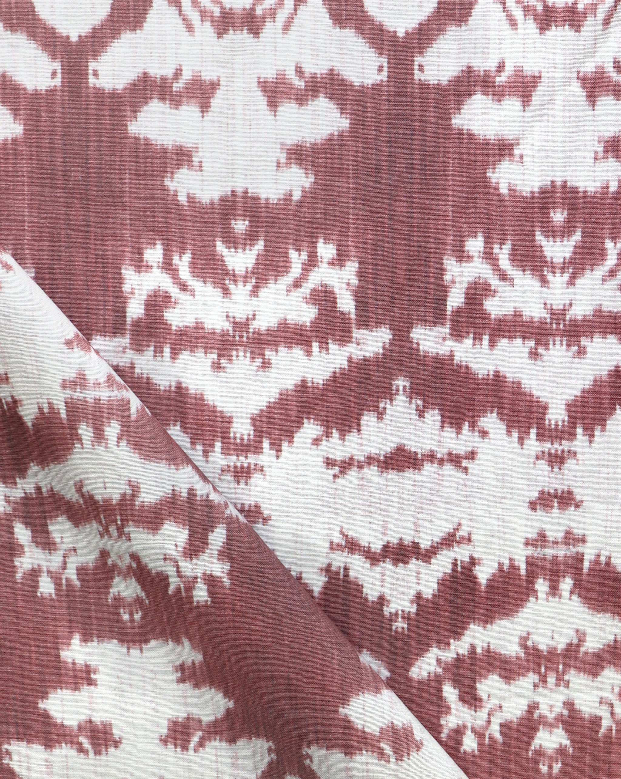 Draped fabric yardage in an abstract ikat print in shades of red and pink on a cream field.