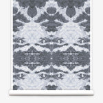 Partially unrolled wallpaper yardage in a painterly ikat print in shades of gray and light blue.