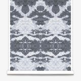 Partially unrolled wallpaper yardage in a painterly ikat print in shades of gray and light blue.