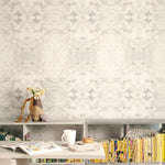 A cluttered desk and bookshelf stand in front of a wall papered in an abstract textural print in cream, gray and tan.