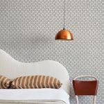 A modernist bed, hanging lamp and chair stand in front of a wall papered in a geometric grid print in gray and white.