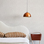 A modernist bed, hanging lamp and chair stand in front of a wall papered in a geometric grid print in cream and white.