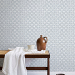 A bench with a towel and clay vases stands in front of a wall papered in a geometric grid print in light blue and white.