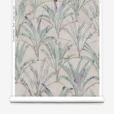 Partially unrolled wallpaper yardage in a painterly palm tree pattern in shades of green and purple on a tan field.