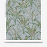 Partially unrolled wallpaper yardage in a painterly palm tree pattern in shades of green and brown on a blue-gray field.