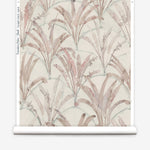 Partially unrolled wallpaper yardage in a painterly palm tree pattern in shades of pink and blue on a cream field.