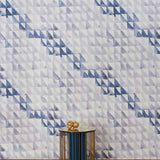 An end table stands in front of a wall papered in a painterly check pattern in shades of blue, gray and white.