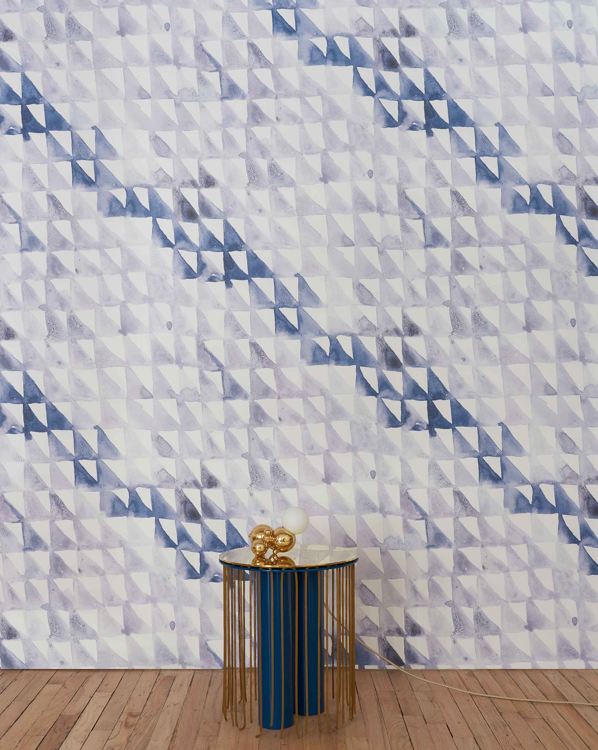 An end table stands in front of a wall papered in a painterly check pattern in shades of blue, gray and white.