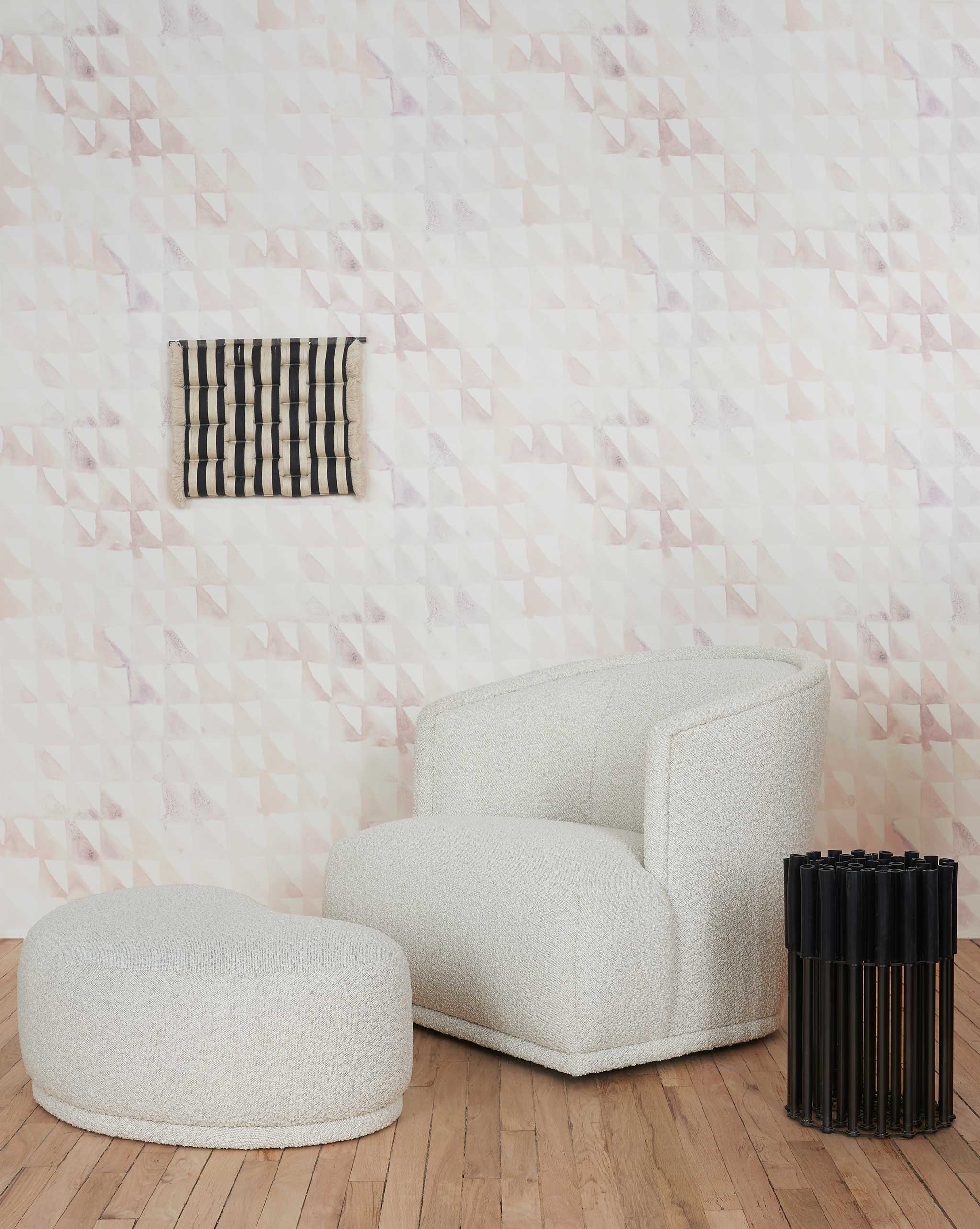 A modernist living tableau stands in front of a wall papered in a painterly check pattern in shades of cream, tan and white.