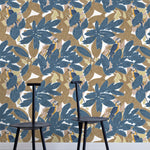 Two minimalist black chairs stand in front of a wall papered in a botanical and parrot print in blue, brown and yellow.