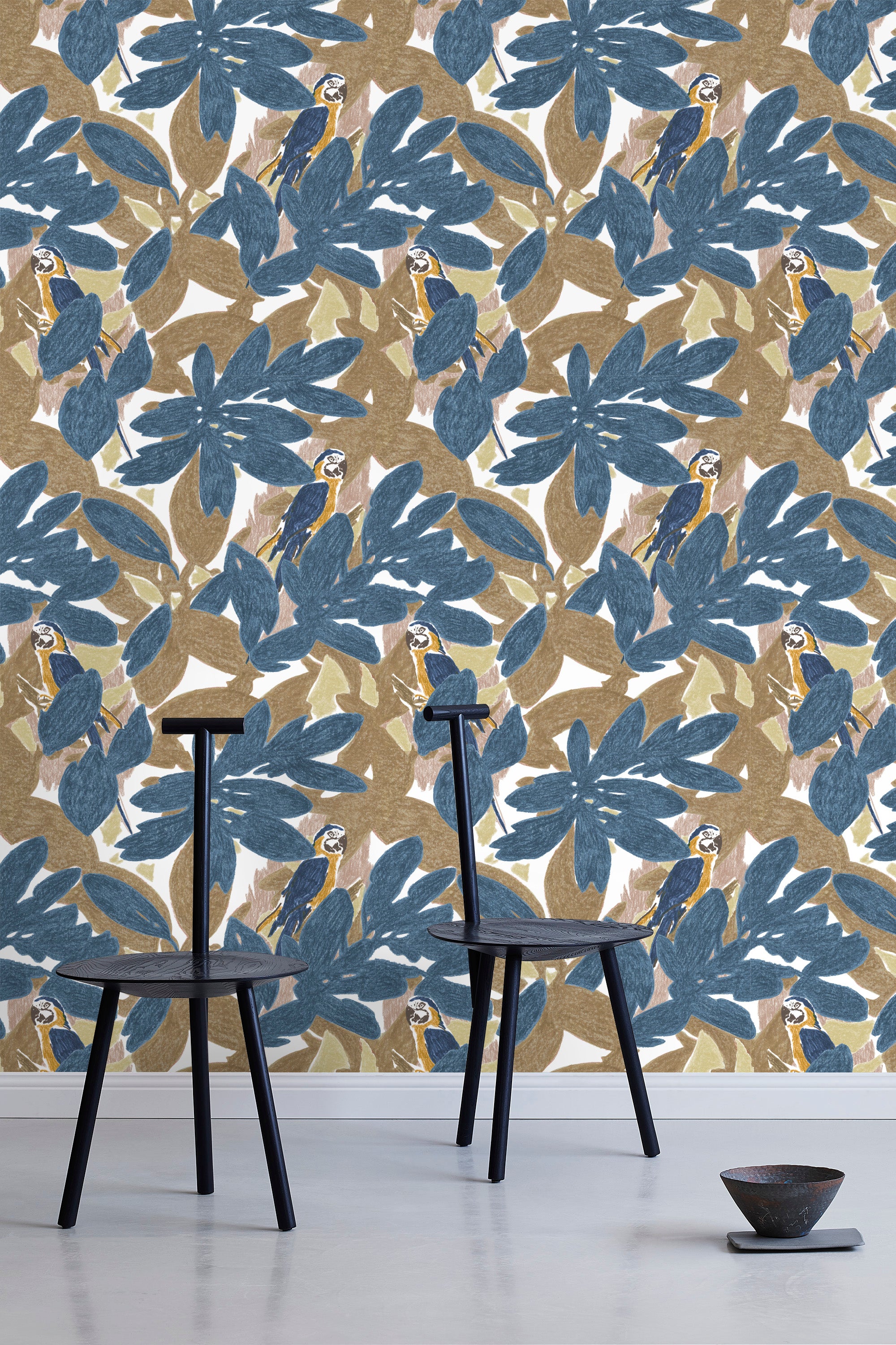 Two minimalist black chairs stand in front of a wall papered in a botanical and parrot print in blue, brown and yellow.