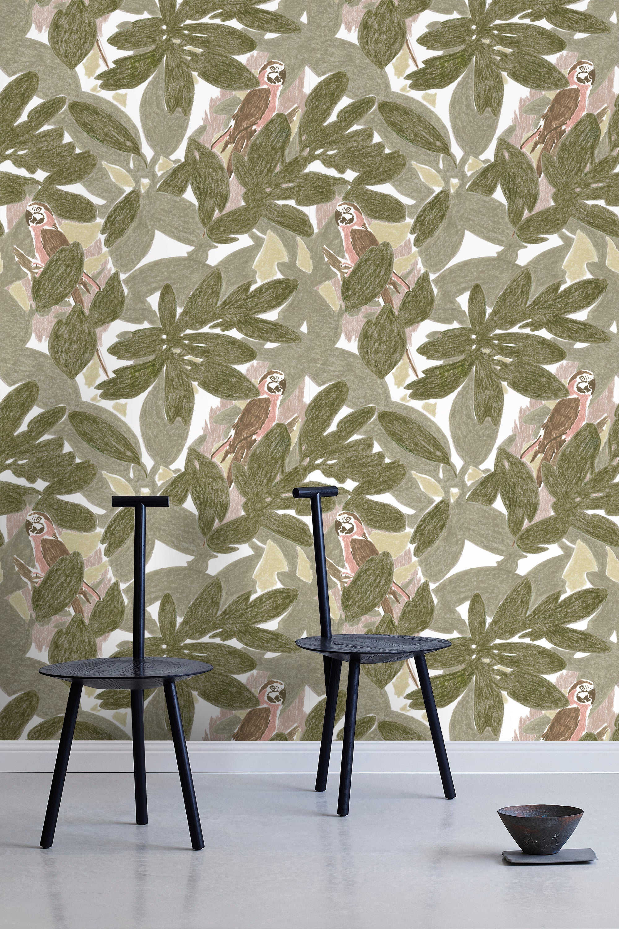 Two minimalist black chairs stand in front of a wall papered in a botanical and parrot print in green, brown and pink.