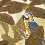 Close-up of fabric in a playful botanical and parrot print in shades of bronze, brown, navy and yellow on a white field.