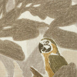 Close-up of fabric in a playful botanical and parrot print in shades of gray, brown and yellow on a white field.